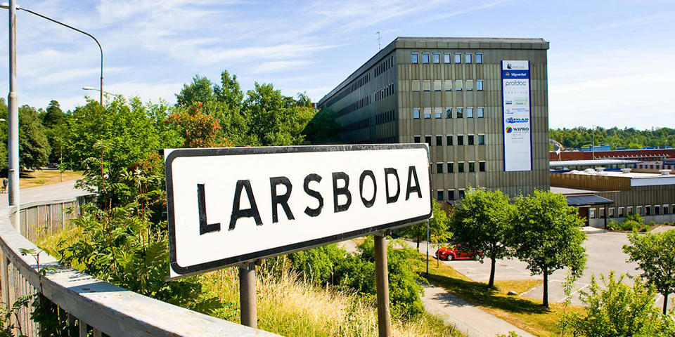 Vy från avfart från Magelungsvägen. Vägmärke med stadsdelsnamnet Larsboda. I bakgrunden flervåningshus, låghus. Parkeringsplats. Foto.