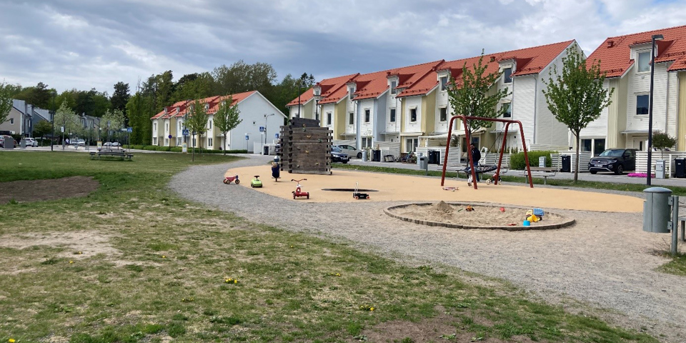 Gräsyta och lekplats framför radhuslängor. På lekplatsen finns sandlåda, klätterställning och gungor. Foto