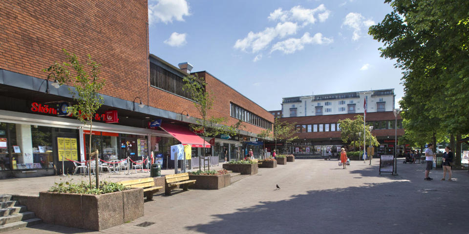 Torg med stor tegelbyggnad bakom. Blå himmel.