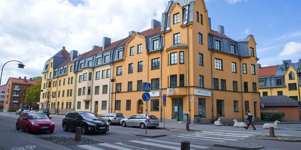 En bilväg med övergångsställe intill flerbostadshus i ljusa färger, foto.