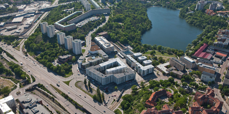 Flygvy över Liljeholmen. Vägar med fordon i rörelse. Bostadsområden, områden för verksamheter och grönområden. En sjö. Foto.