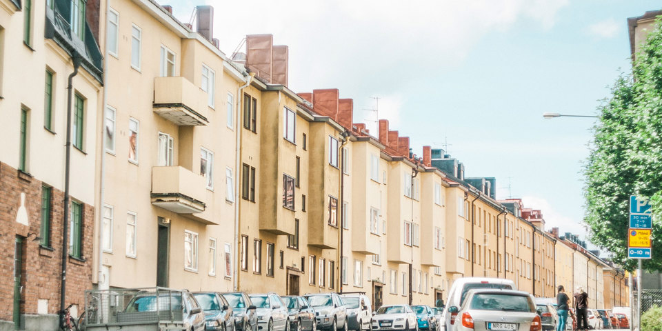 Gata med flerbostadshus i ljusa färger. Bilar  finns parkerade på gatan, foto.
