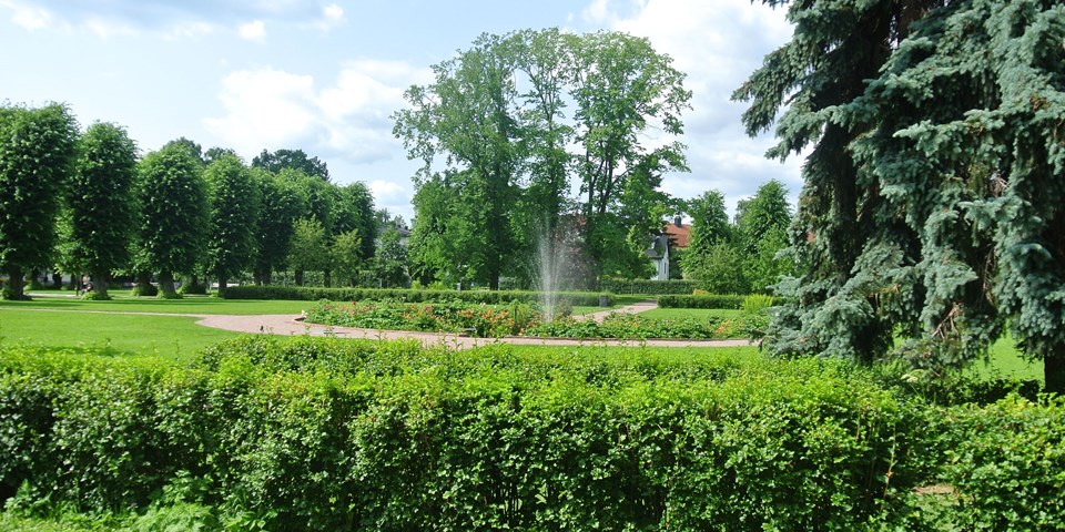 Lummig park med gräsytor, träd och buskar. I mitten finns en fontän, foto.