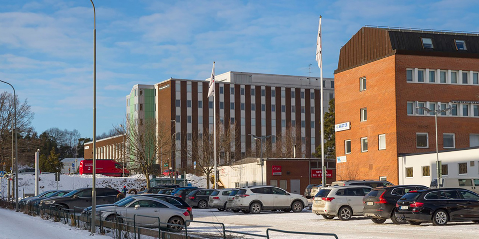 Kontorshus med bilparkering utanför. Flera parkerade bilar. Foto.
