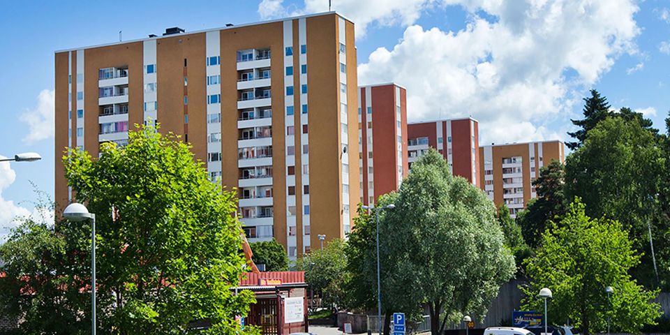 Bostadshus med flera våningar. Omgivande träd. Foto.