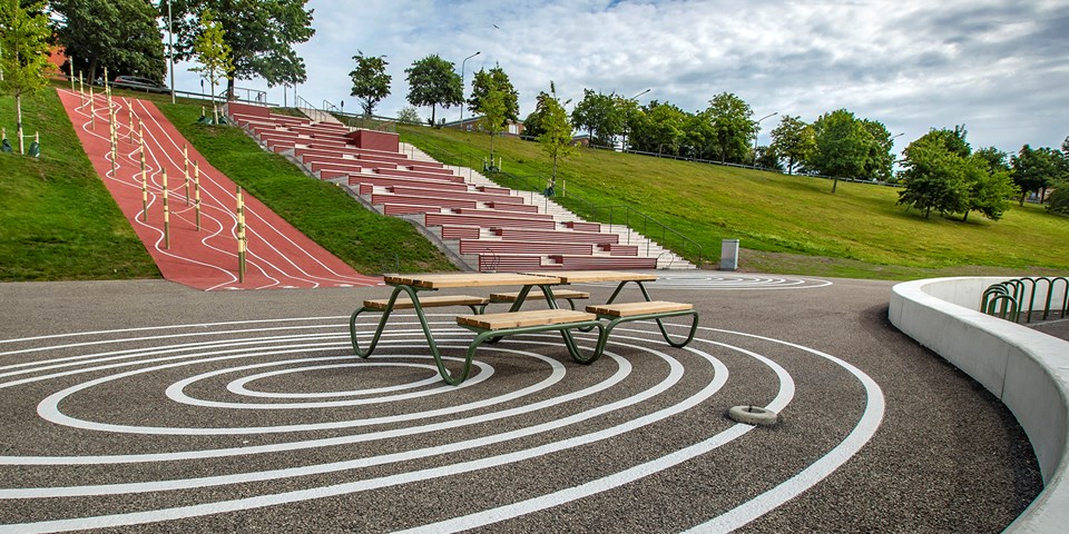 Park med bänkar, trappor och aktivitetsytor i slänten. Foto.