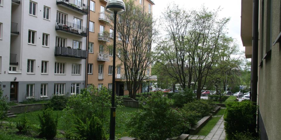 En liten park omgiven av flerbostadshus med stenbelagda gångar. Foto.