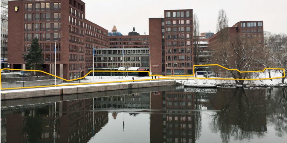 Kontorshus i tegel i flera våningar. Husen speglar sig i det intilliggande vattnet. Gula markeringar är inritade mellan husen och vattnet. 