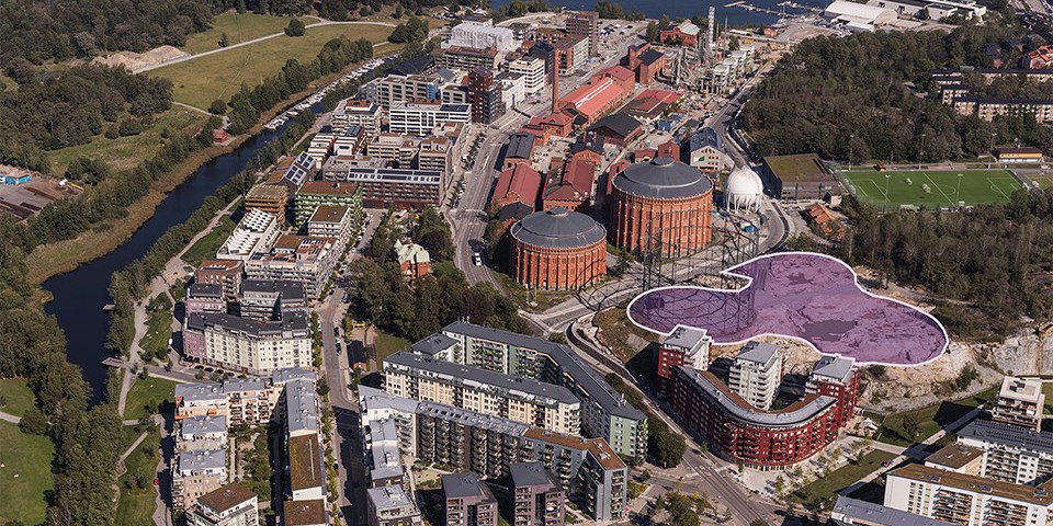 Natur- och grönområden, vatten, bostadshus, gasklockor och fotbollsplan. Flygfoto.