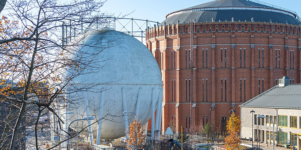 Gasklocka med tegelfasad, vit sfär, skola och skolgård med  lekande barn. Foto.