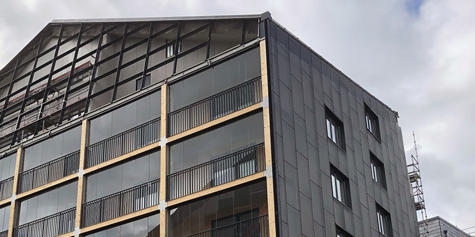 Plusenergihus i svart med solpaneler och balkonger. Byggnadsställningar runt huset. Foto.