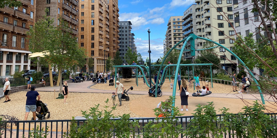 Lekplats i Norra Stationsparken omgiven av flerfamiljehus med barn och vuxna som leker och promenerar. 