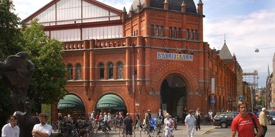 Östermalms torg med människor i rörelse och saluhallen i bakgrunden, foto.