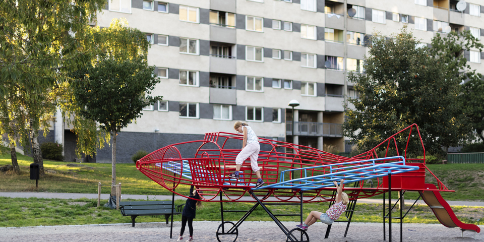 Klätterställning i form av ett flygplan i park vid bostadshus och träd. Barn som klättrar, foto.