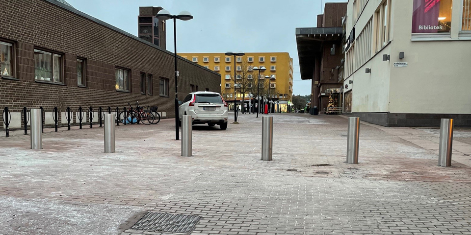 En gata kantad med hus och en bil stående på gatan. Pollare i förgrunden, foto.