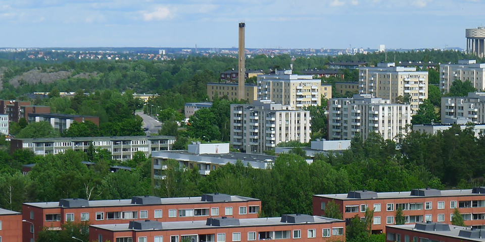 Höga bostadshus med flera våningar och balkonger med omgivande träd och berg. Foto.