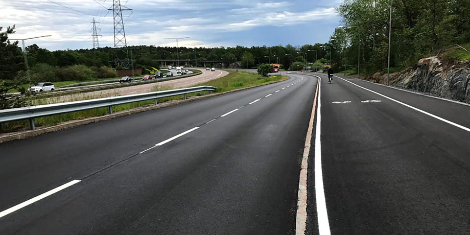 Bilväg med cykelbana och trottoar. Foto.
