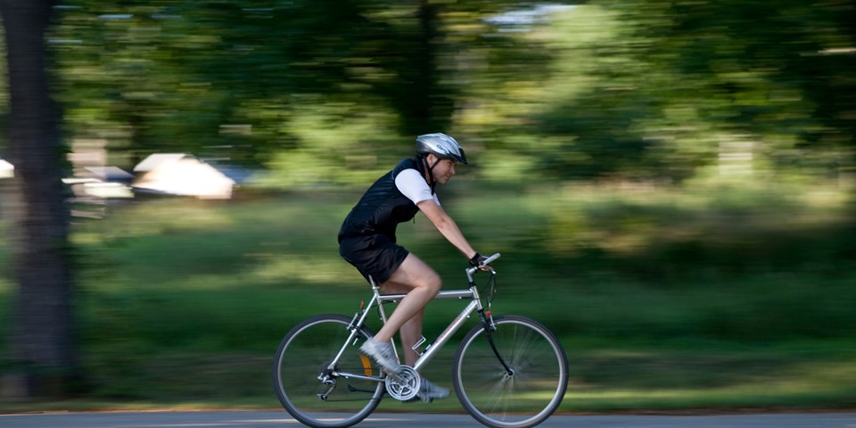 En cyklist som cyklar på en väg genom grönområde, sett från sidan, foto.