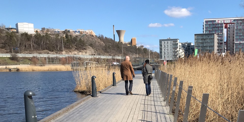 Två personer syns bakifrån, gåendes på en strandpromenad, fotografi.