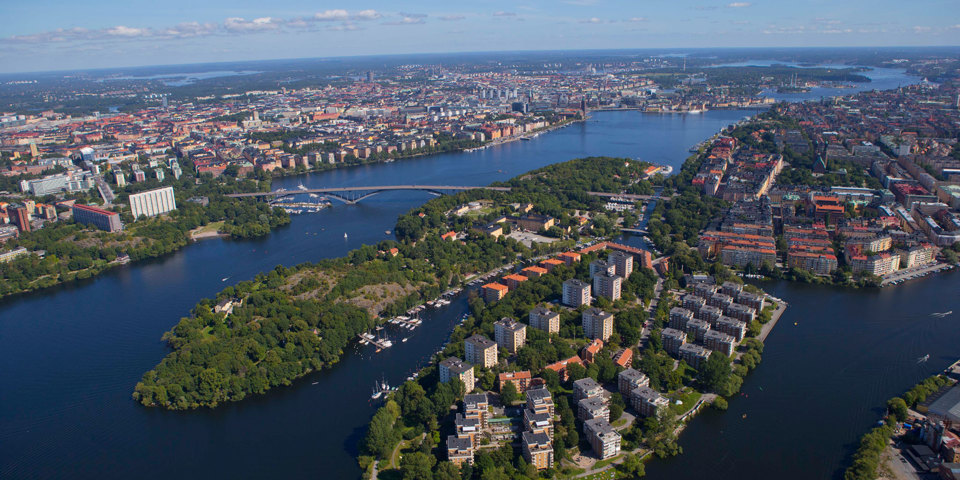 Flygfoto över område med hus, grönområden och vatten. 