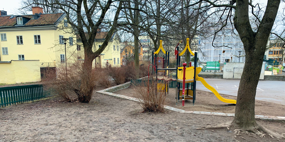 Lekplats med sandlåda med omgivande flerbostadshus och träd, fotografi.
