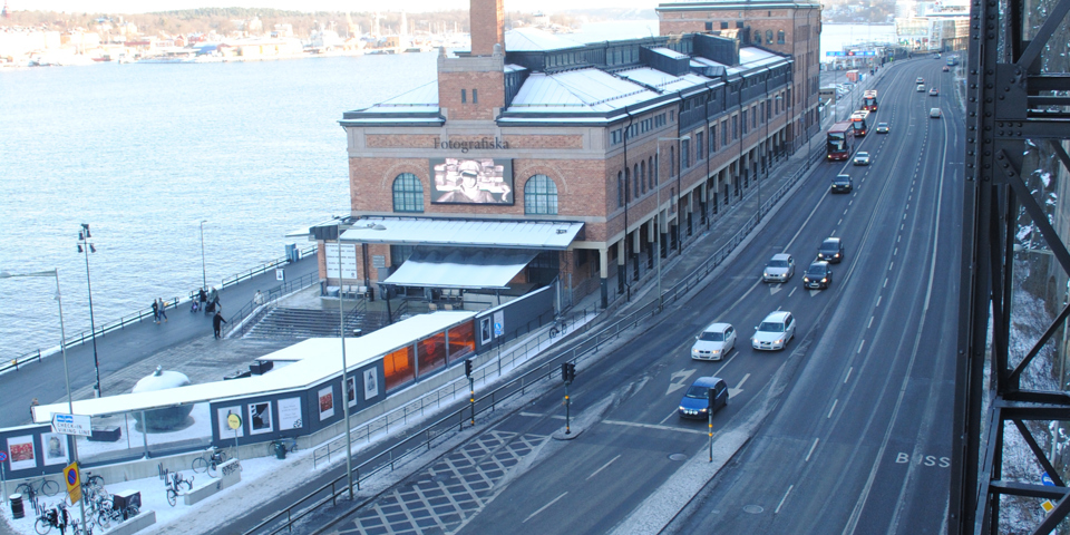 Fotografiska muséet, bilväg med bilar och buss som kör, vatten och människor i rörelse. Foto.