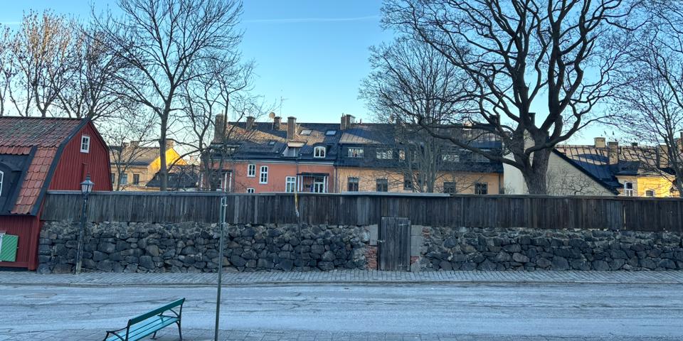 En gammal stenmur i svarta stenar längs Stigbergsgatan i Stockholm. Bilden visar murens struktur och omgivande fastigheter.