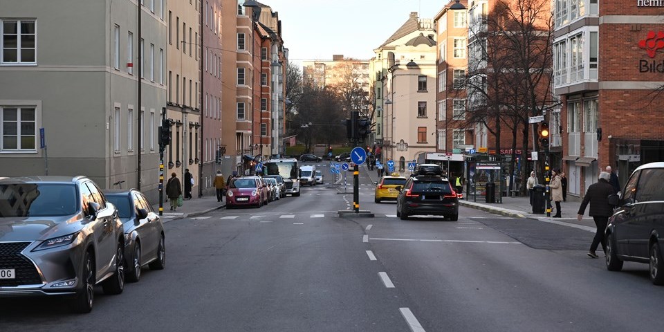 Foto över Rosenlundsgatan med biltrafik och omgiven av bostadshus och andra byggnader. 