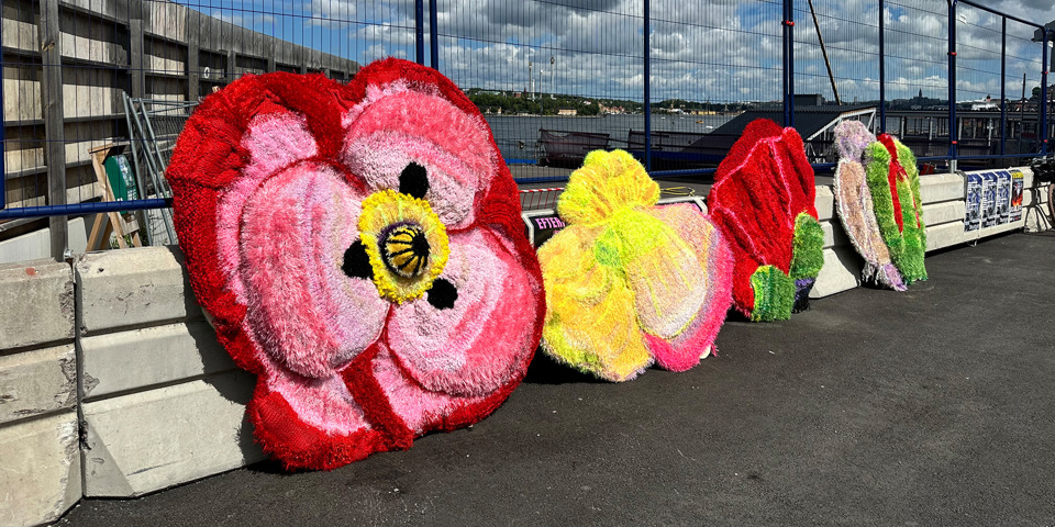 Stora stickade blommor i rosa och gula nyanser vilar mot ett byggstaket.