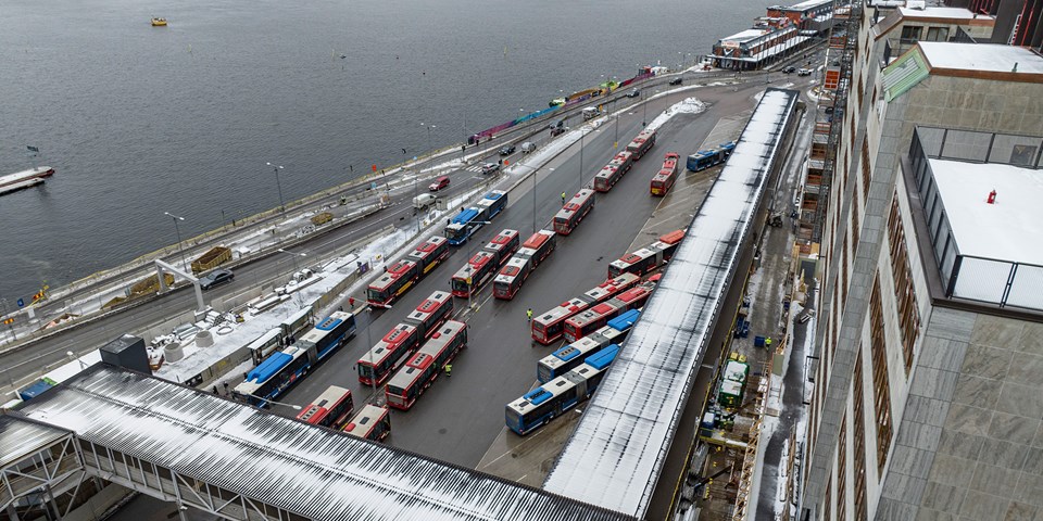 Vy över en bussterminal på Stadsgården vid Slussen. Flera röda och blåa bussar är i rörelse eller står parkerade intill terminalens ankomst- och avgångsplatser.
