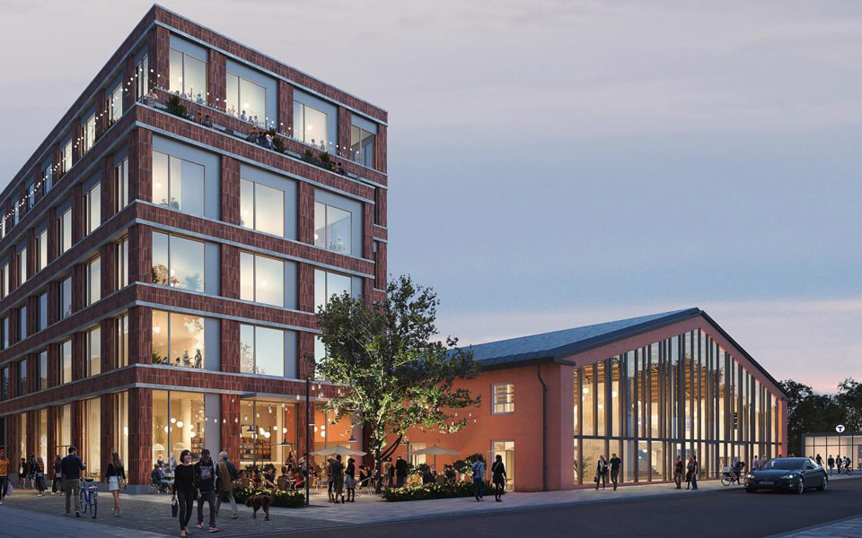 En modern byggnad med stora glasfönster och flera våningar, bredvid en renoverad industribyggnad, omgiven av människor som promenerar och sitter på en uteservering på kvällen.