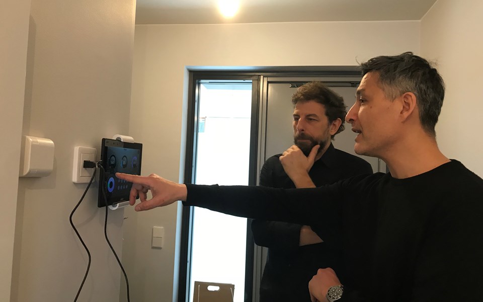 Två män tittar på en digital skärm på väggen som är kopplad till en strömbrytare.