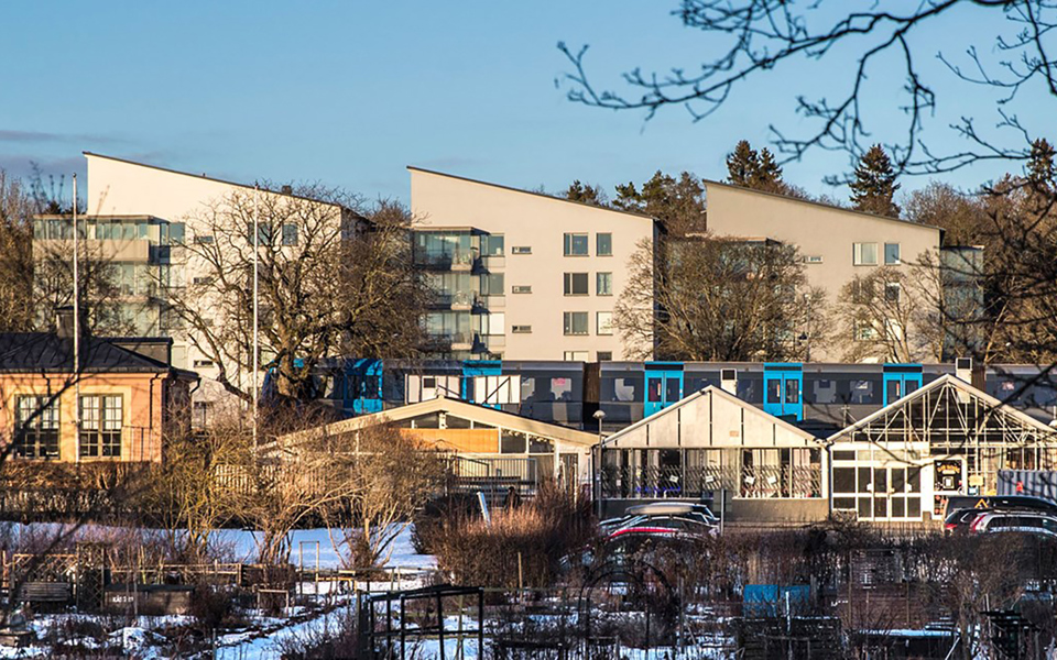 Kolonilotter, bostadshus, bilparkering och tunnelbana. Foto.