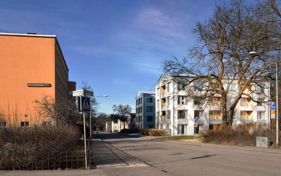 Flerbostadshus till höger, till vänster syns en skolbyggnad, bilväg, fotomontage.