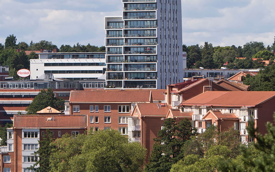Bostadshus med flera våningar och stora balkonger samt kontorslokaler med omgivande träd och vatten. Foto.
