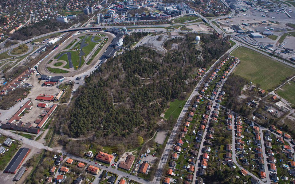 Flygvy över bostadshus, skogsområde, bilvägar och gräsytor, foto.