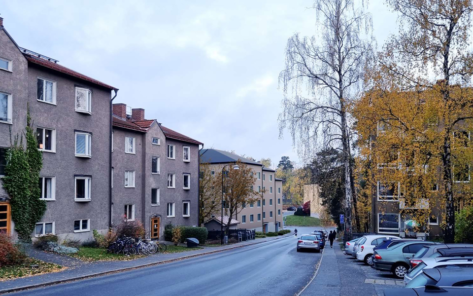 Flerbostadshus längs med gata, parkerade bilar, fotomontage.