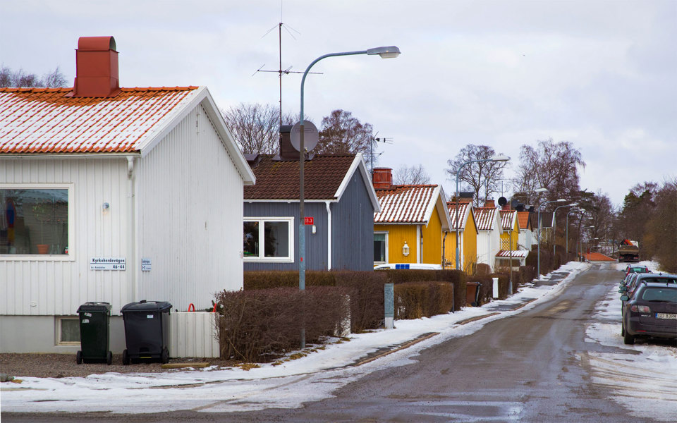 Småvillor i olika färger på rad på en gata, lite snö på marken, parkerade bilar, fotografi.