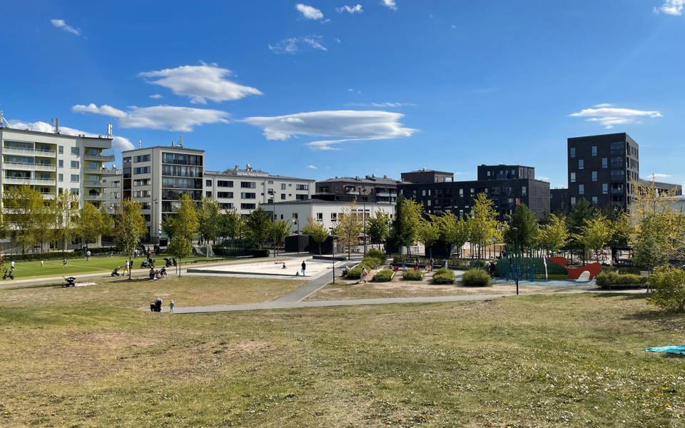 Gräsplätt och längre bort fotbollsplan, lekpark och vita och svarta flerbostadshus.
