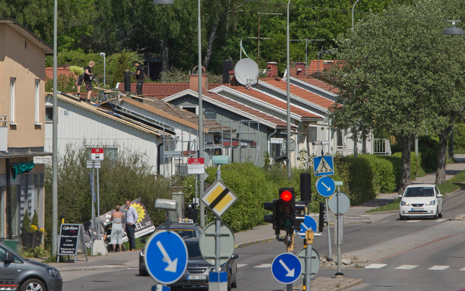 Gata i bostadsområde med trafikljus och vägskyltar. Gatan är  kantad av villor och träd, foto.