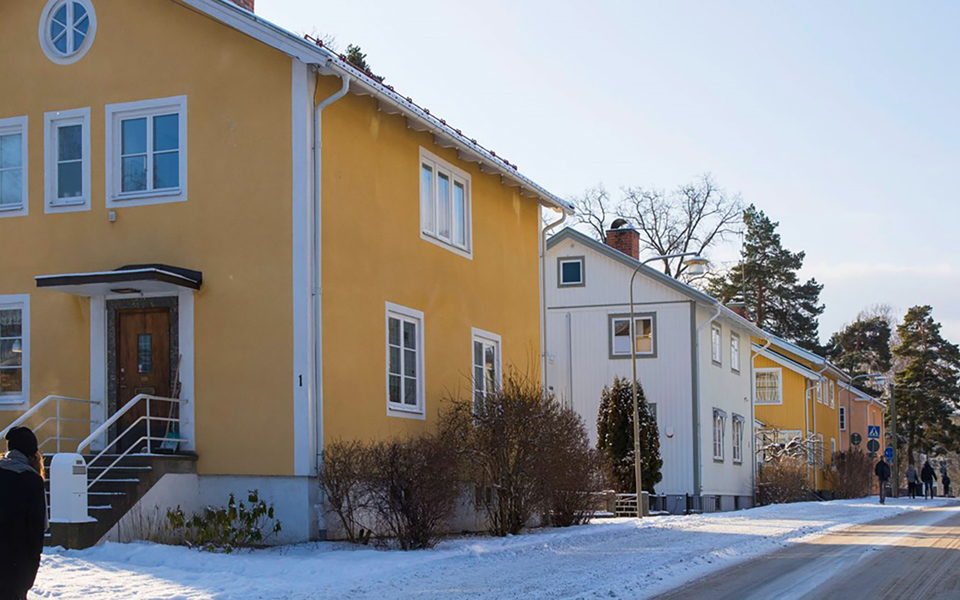 Villor vid bilväg. Människor som promenerar på trottoar. Foto.