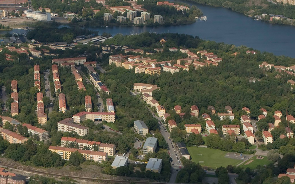 Bostadshus, skog, fotbollsplan och vatten. Foto.