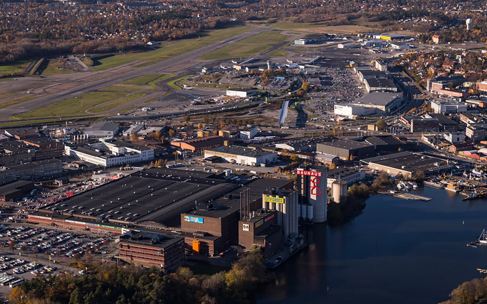 Industribyggnader som ligger vid vattnet. Stora bilparkeringar med flera parkerade bilar. Foto.