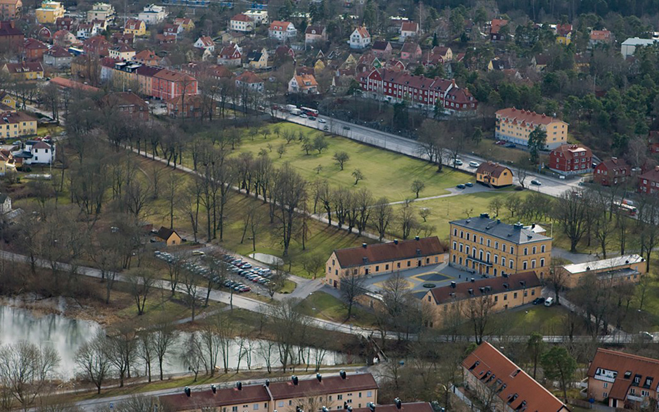 Ulvsunda slott som ligger vid vattnet. Bostadshus, stora gräsmattor och träd. Foto.