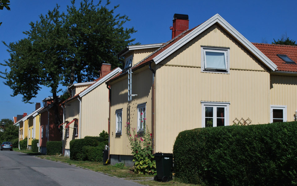 Vy över en villagata där ena sidan av gatan syns. Fem villor på rad. Träd, häckar, rabatter. Foto.