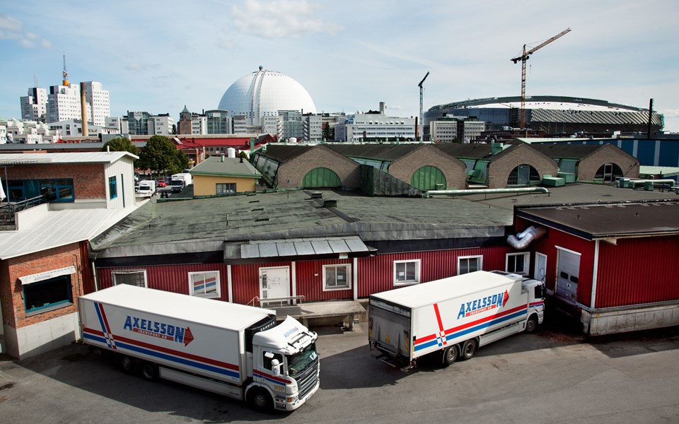 Varuintag på baksidan av låg byggnad. Två lastbilar. I bakgrunden flera byggnader samt Globen och Tele 2 Arena.  Foto.
