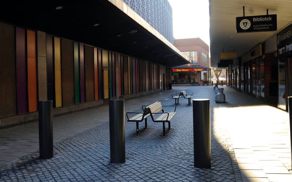 Pollare och sittbänkar vid gång i centrum med verksamheter längs med, fotografi.