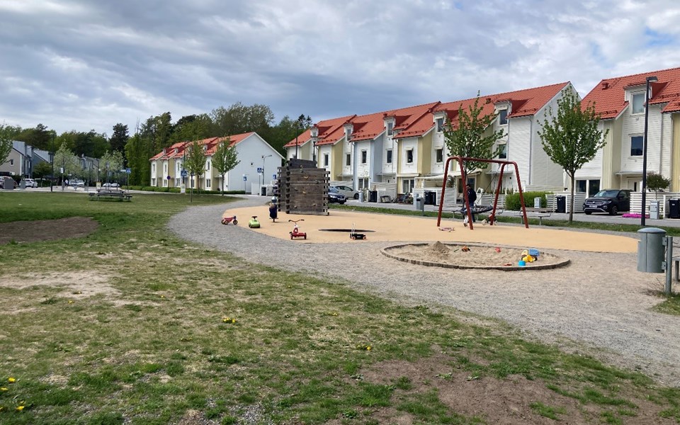 Gräsyta och lekpark framför radhuslängor. På lekplatsen finns sandlåda, klätterställning och gungor. Foto
