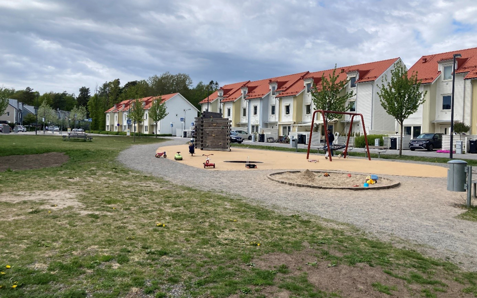 Gräsyta och lekplats framför radhuslängor. På lekplatsen finns sandlåda, klätterställning och gungor. Foto