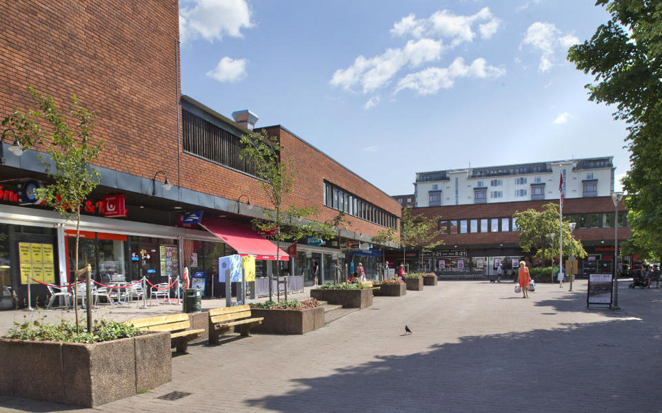 Torg med stor tegelbyggnad bakom. Blå himmel.